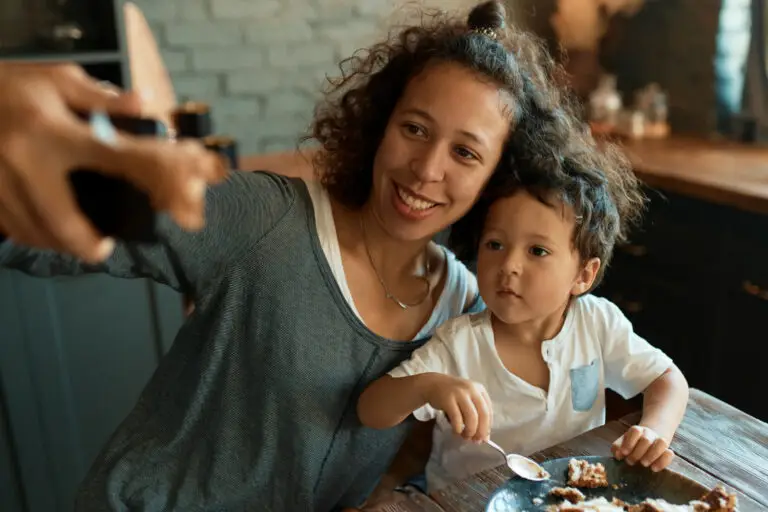 A mother and young son smiling together while sitting at a table.