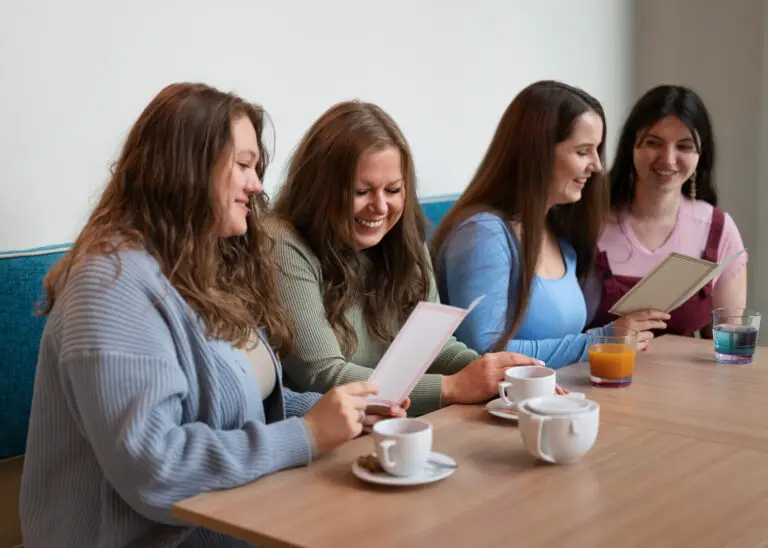 Three women smiling and talking while sitting at a cafe table with coffee.