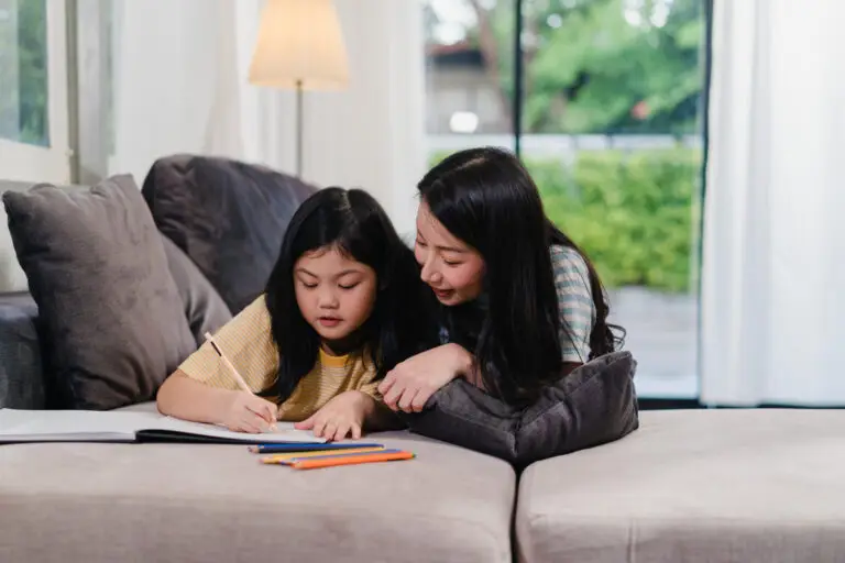 A mother and daughter sitting on a sofa while looking at a book together.